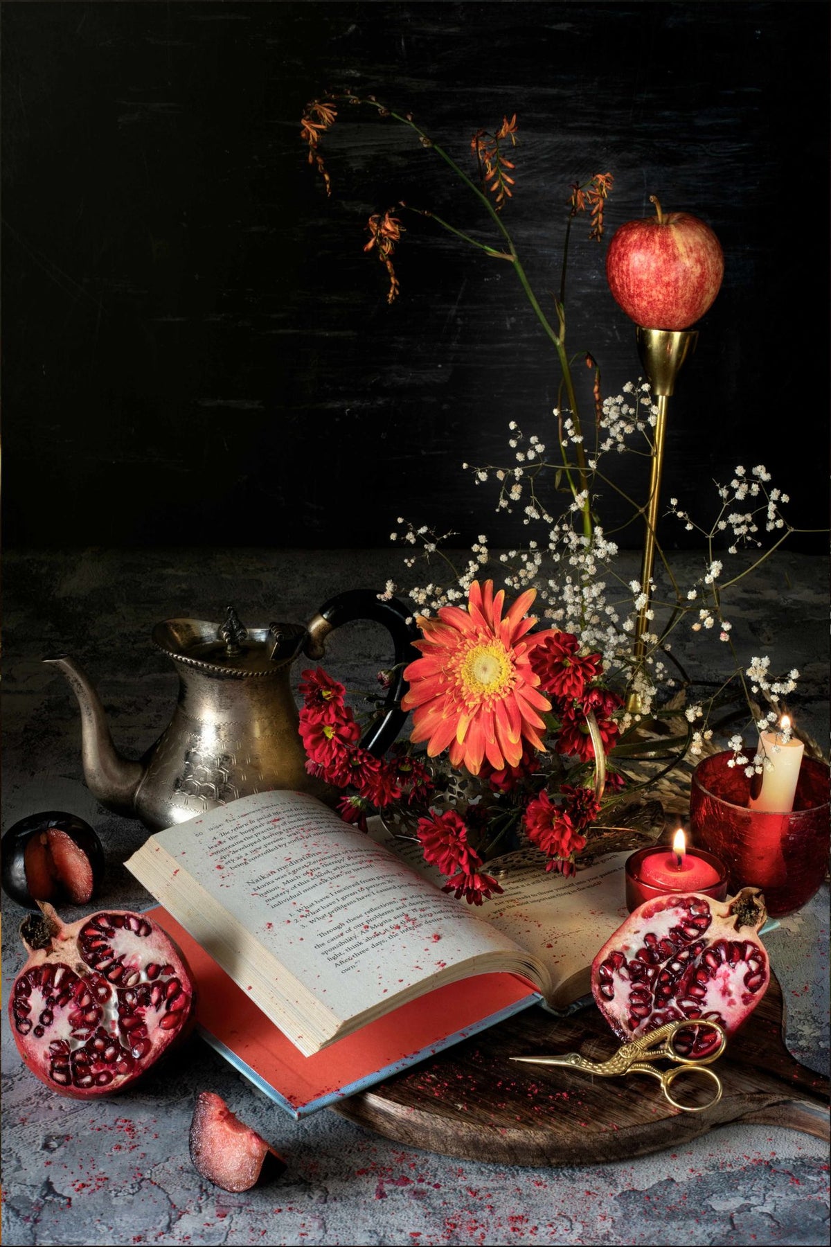 Joyful Passion (2022) - Open red book with pomegranates, silver teapot, orange gerbera, red chrysanthemums and lit candles, fine art print by Stillness by Sheetal